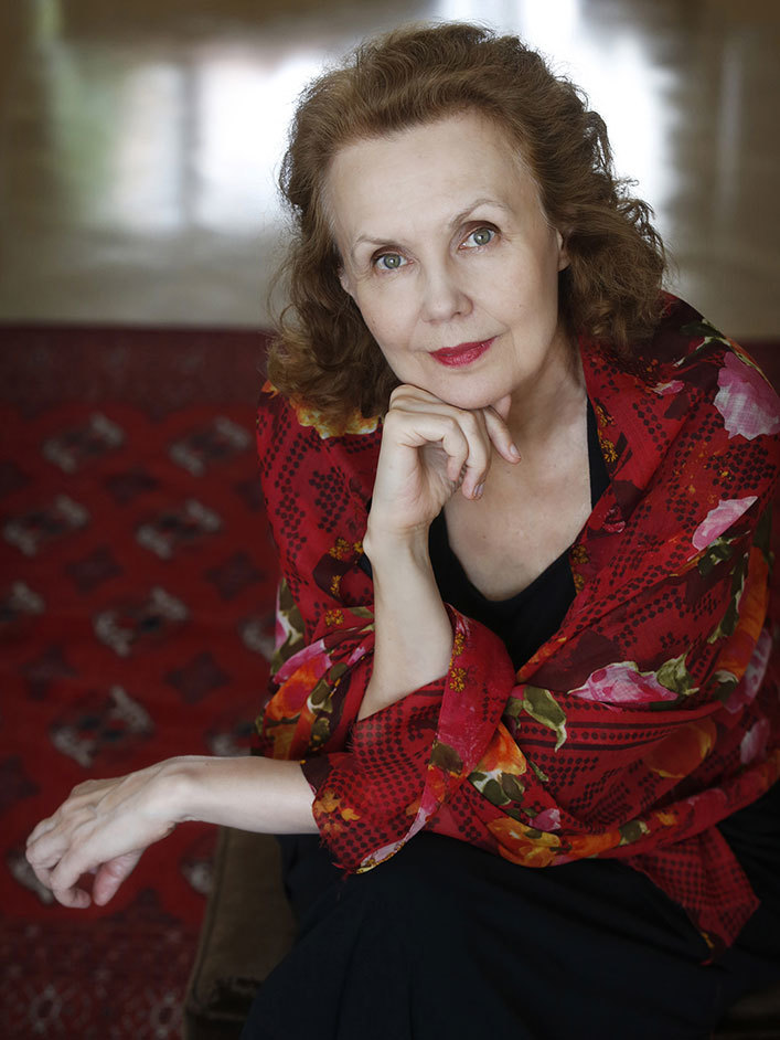 Kaija Saariaho sitter foran et mørkerødt teppe