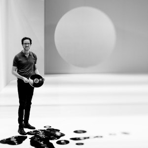 Svart-hvittbilde av Erik Dæhlin som står i et stort hvitt rom og holder vinyler