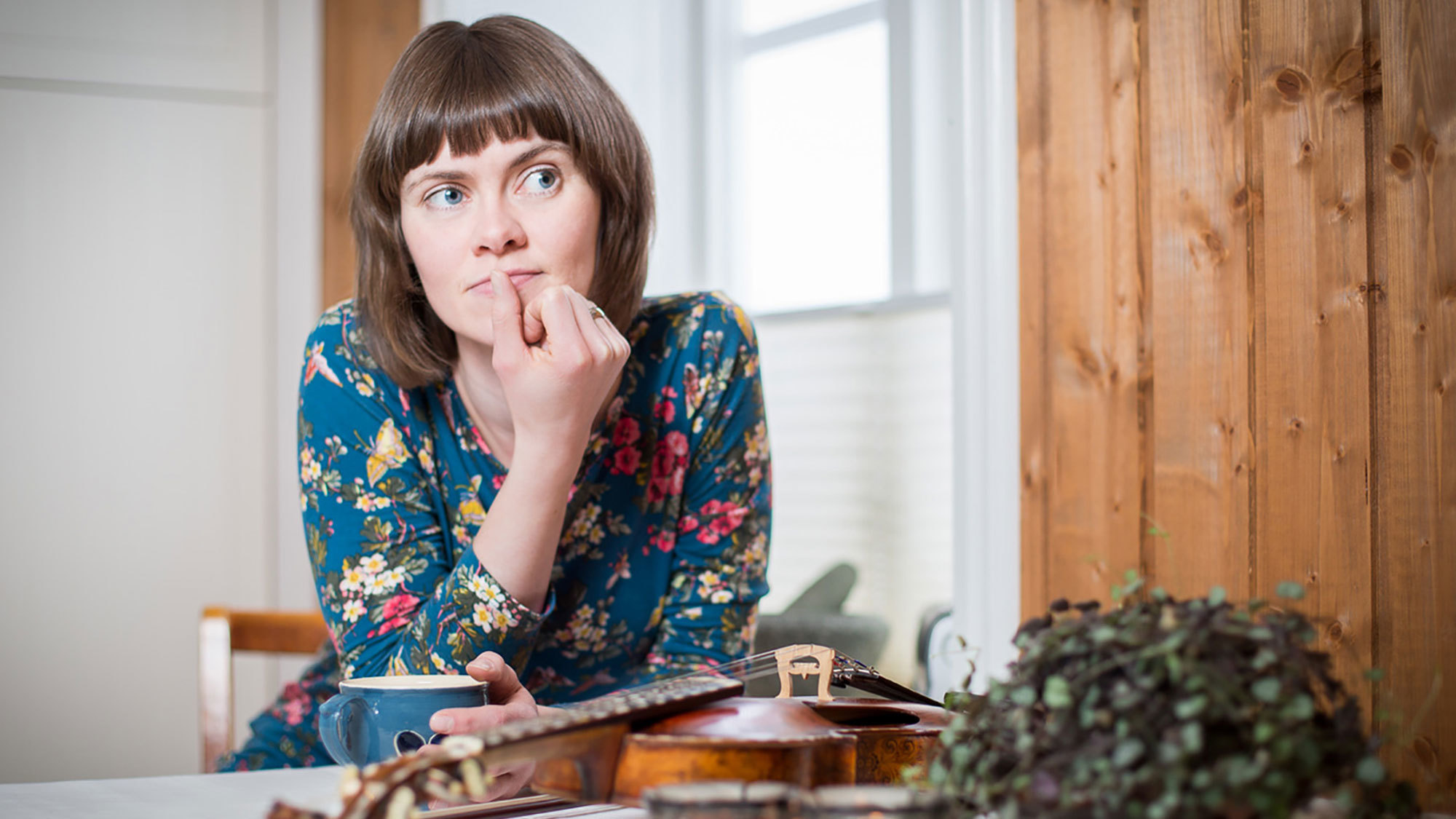 Gro Marie Svidal sitter ved bord med hånda på haka og ser tankefull ut. Fela ligger på bordet.