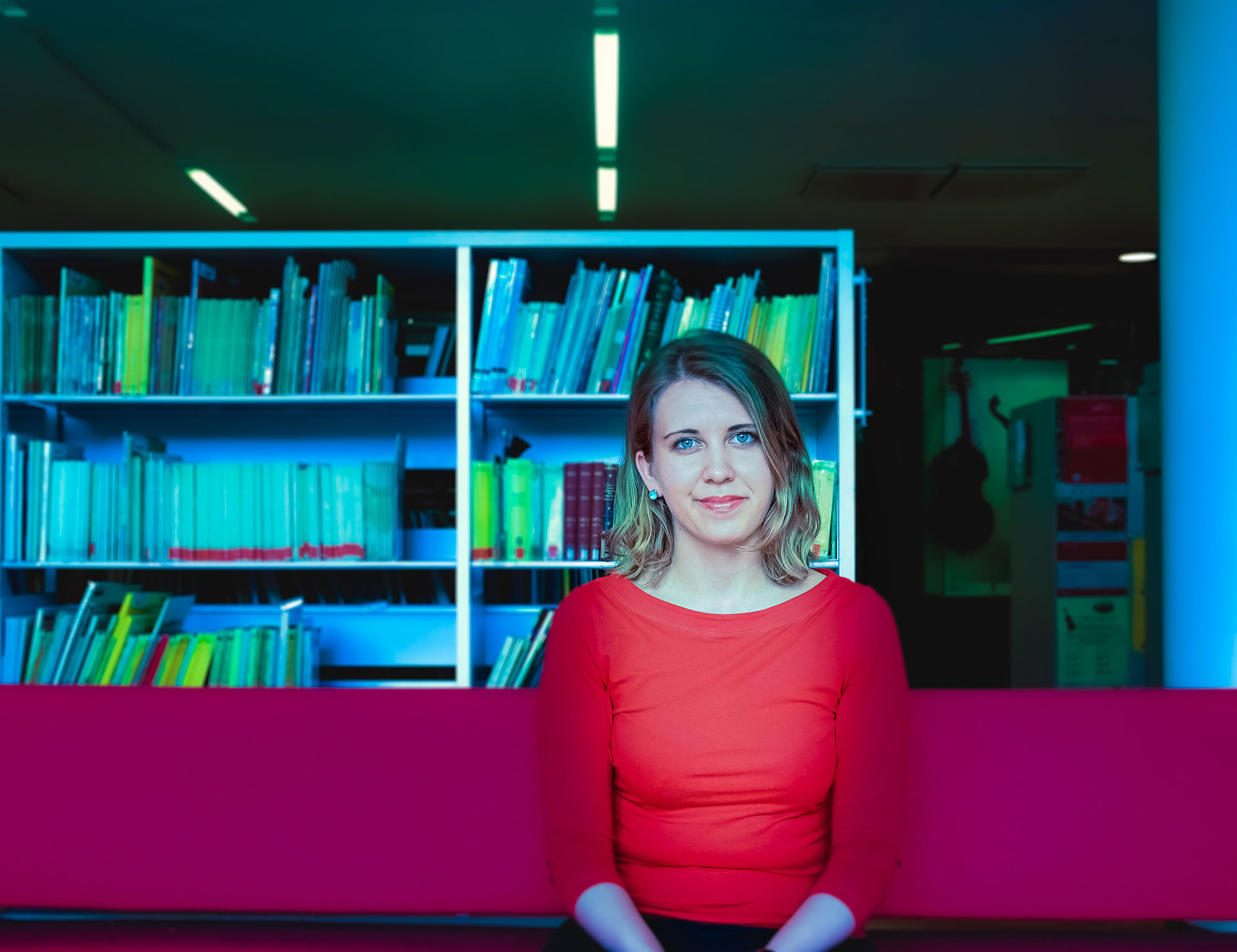 Aliisa Neige Barriere sitter foran en hylle i biblioteket på NMH.