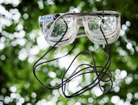 Arne Nordheims briller liggende på et speil hvor trær reflekteres.