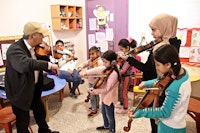 Barn med hver sin fiolin står vent mot en underviser.