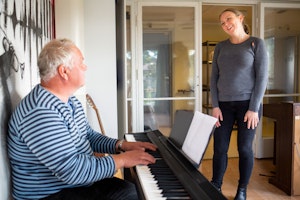 Homeside-deltaker Harald spiller piano mens Kristi Stedje ser på