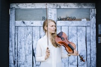 Karin Hellqvist is standing in front of an old wood door holding her violin.