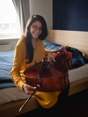Cellist María Alejandra Conde Campos sitter på seng og skrur på celloen sin