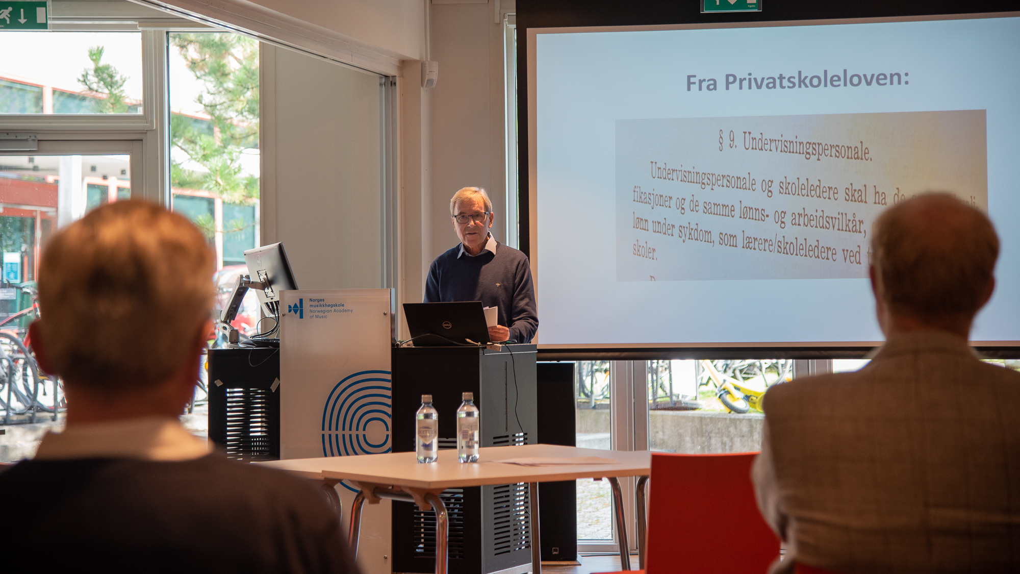 Fra seminaret om NMHs historieprosjekt. Einar Solbu på talerstolen foran en skjerm som viser utdrag av privatskoleloven.