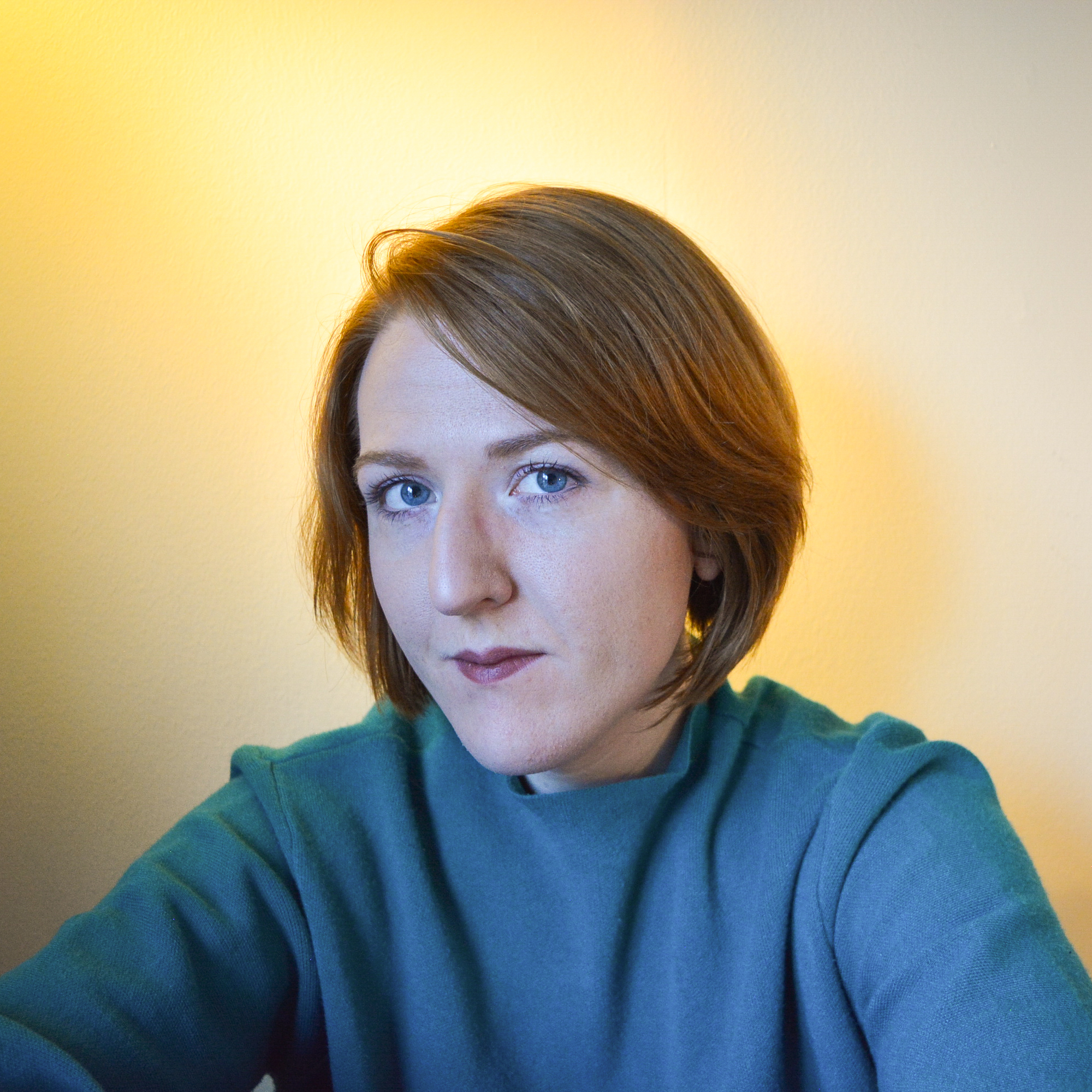 Isa is sitting in front of an empty wall and looking into the camera.