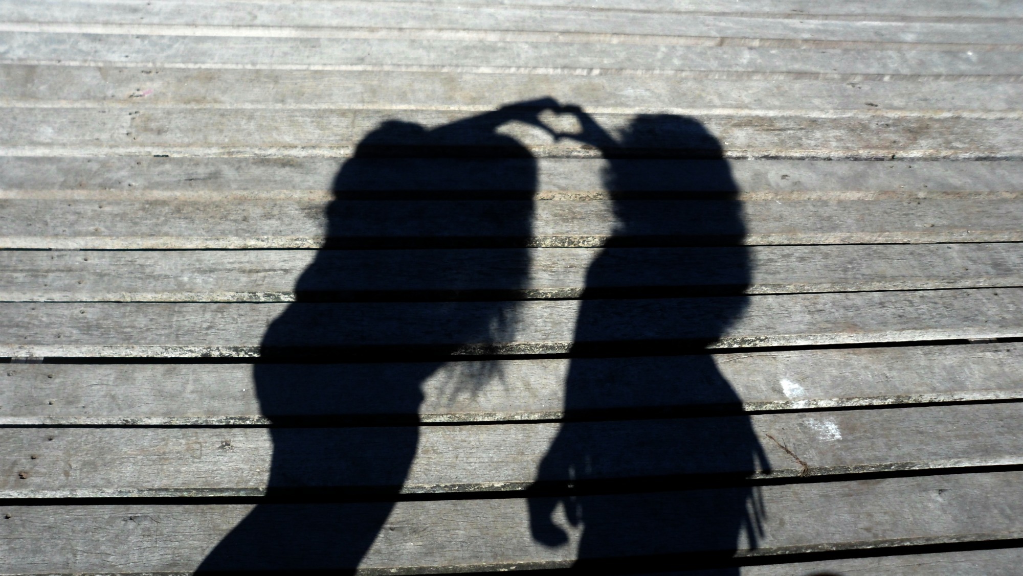 Skyggen av to personer som lager et hjerte med hendene, foran en vegg.