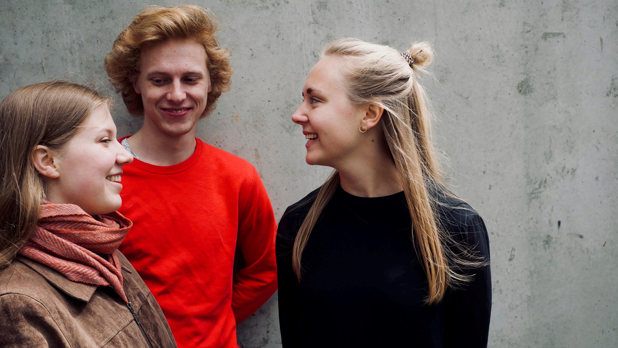 Kongle Trio står og smiler til hverandre foran betongvei