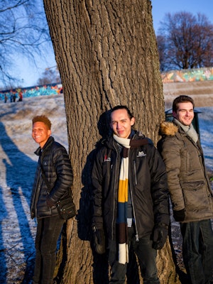 Utvekslingsstudentene Uviwe Caso, Levan Chkhaidze og Eduardo Villamizar står foran et tykt tre i snødekt landskap og smiler.