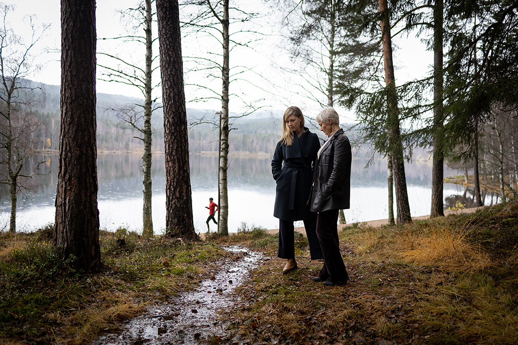Live Maria Roggen og Ingfrid Breie Nyhus i skogen med vann og en jogger i bakgrunnen