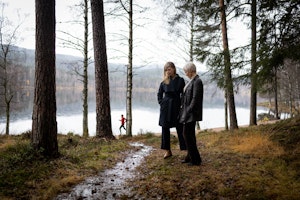 Live Maria Roggen og Ingfrid Breie Nyhus i skogen med vann og en jogger i bakgrunnen