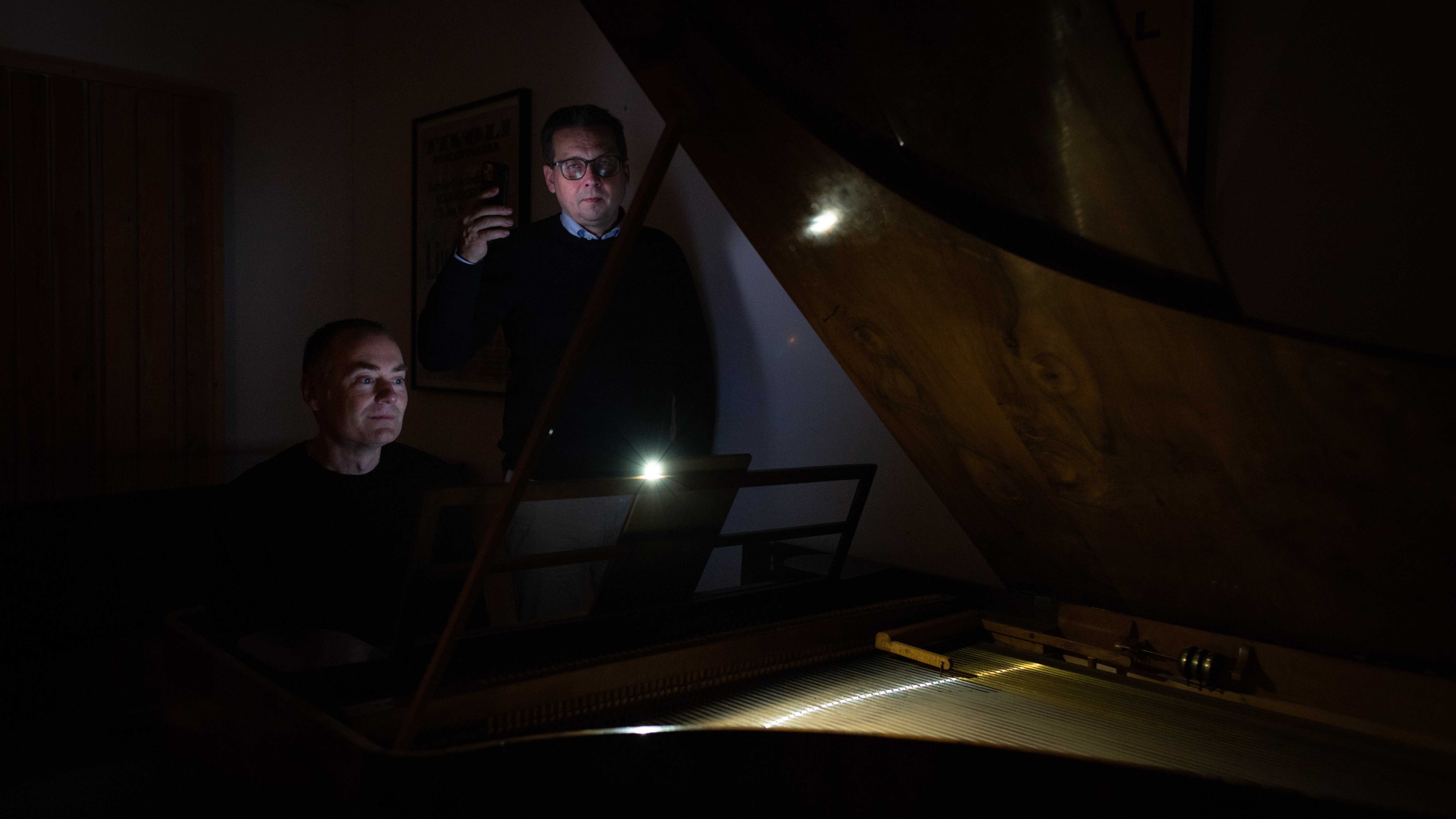 Gunnar Flagstad og Frank Havrøy med lommelykter ved flygel i mørkt rom