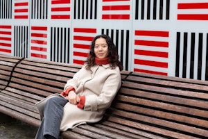 Susanne Trinh på benk foran vegg i rødt og svart