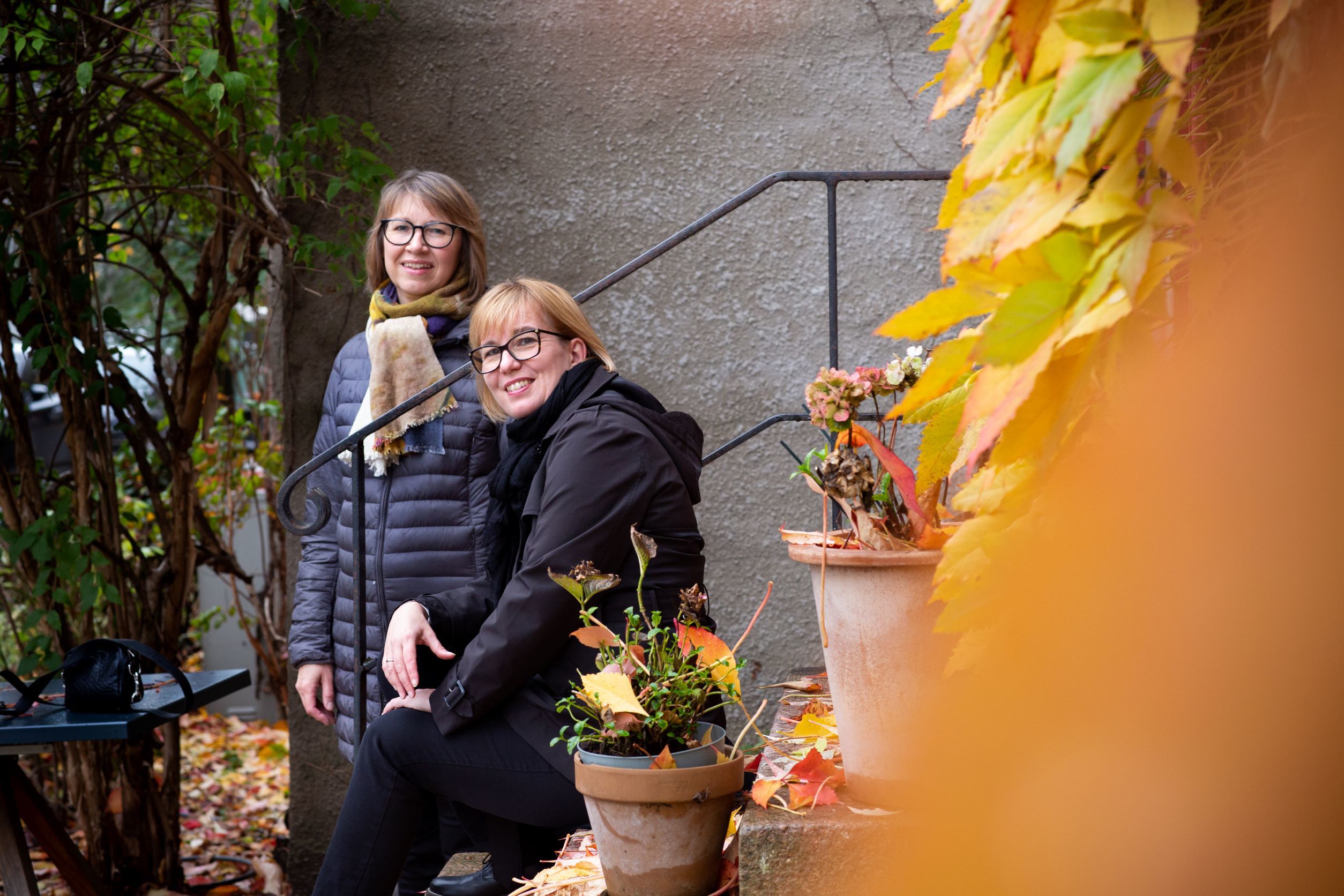Siw Graabræk Nielsen og Sidsel Karsel sitter på/står ved trapp, høstblader i forgrunnen