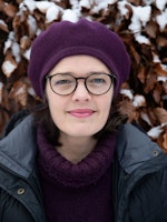 Astrid Kvalbein med alpelue foran brune blader med snø på.