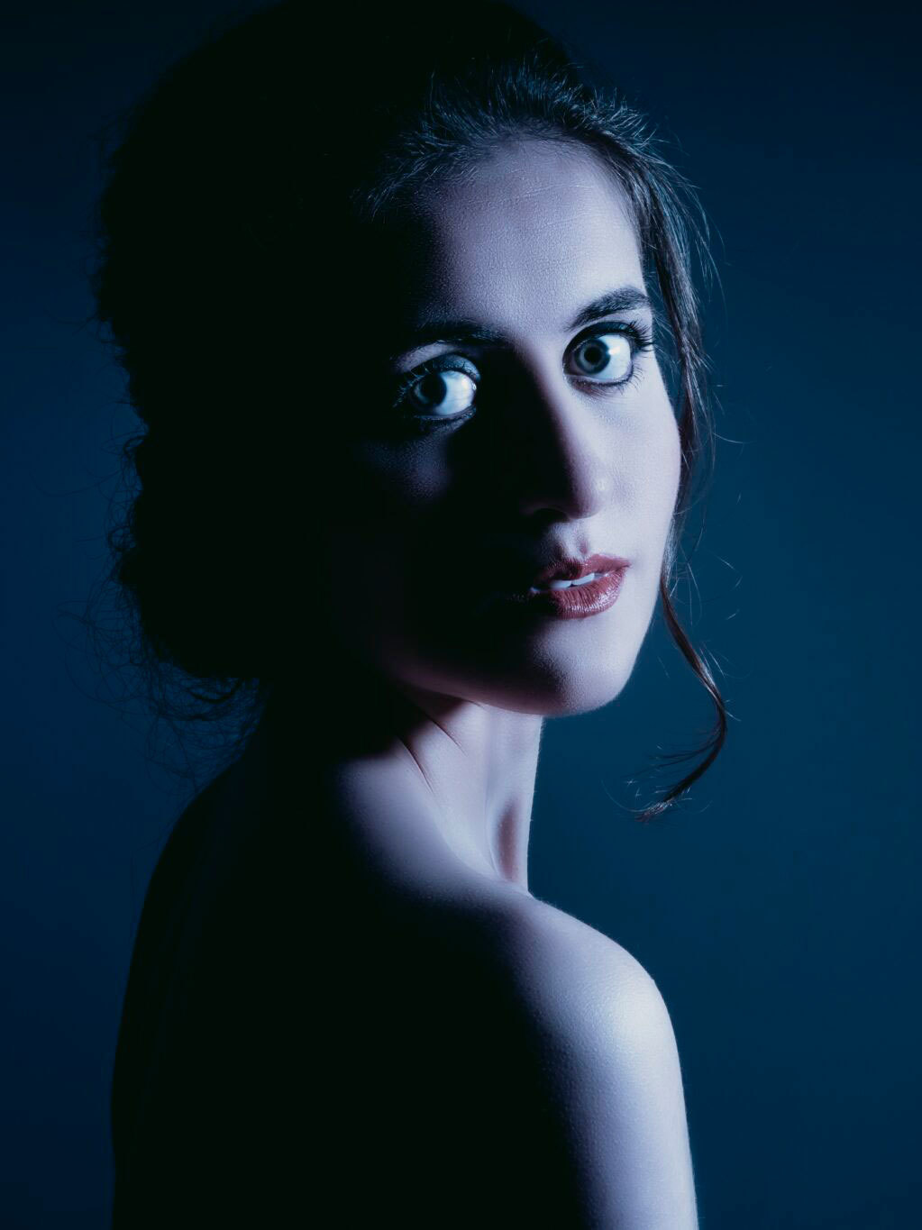 Mørkt portrett av harpist Claudia Lamanna med blålig lys.