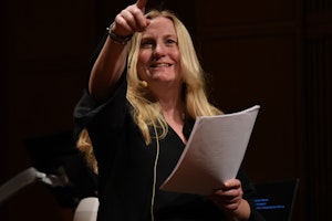 Sigrid Røyseng med papirer i hånden, peker ut mot salen