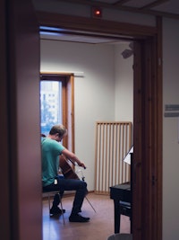 Cellist sitter på et øverom og spiller med ryggen til.