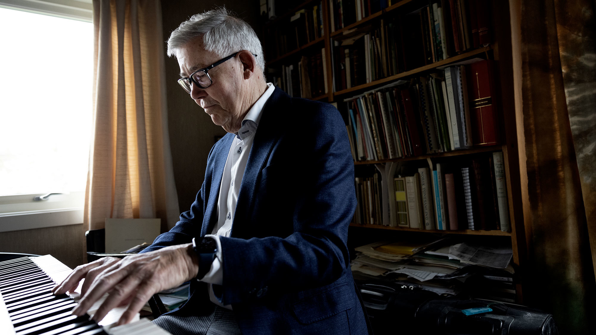 Harald Herresthal som sitter ved orgelet og spiller, med bokhyller bak seg.