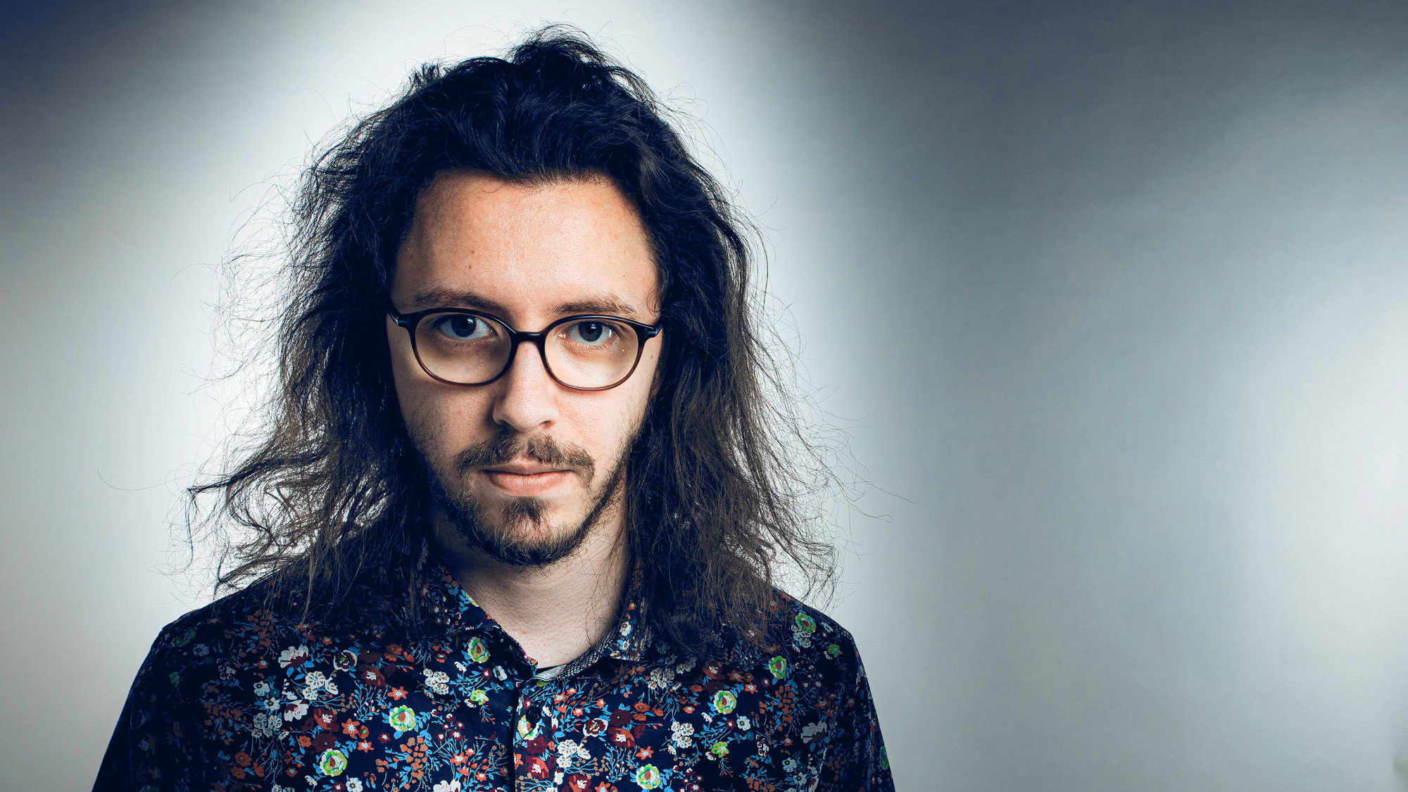 Portett av Morten Georg Gismervik, med langt hår, briller og mønstrete skjorte.