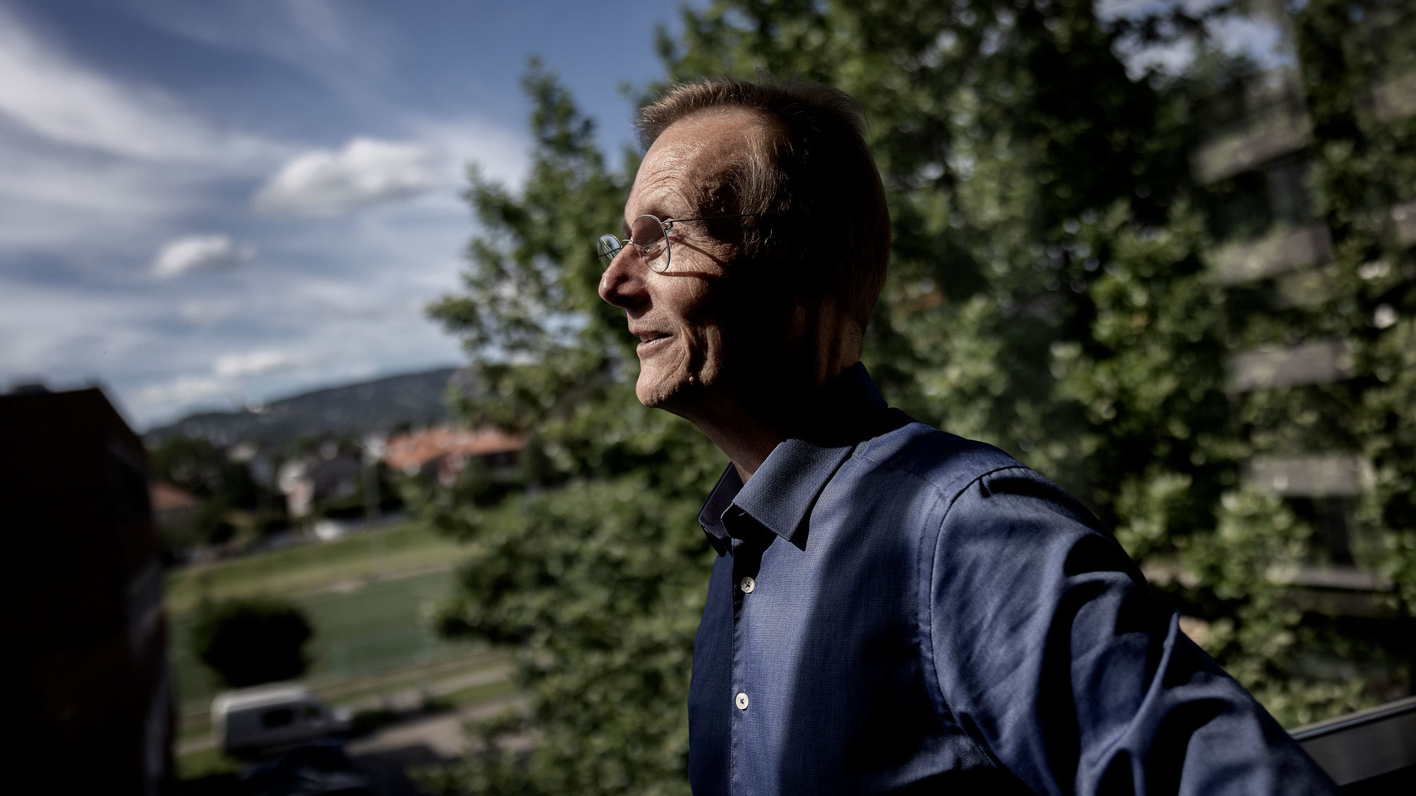 Peter Tornquist står og ser utover området. Det er blå himmel og grantrær bak ham.