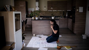 Idin Samimi Mofakham sitter på gulvet foran kjøkkenet sitt og skriver på notatene sine i farger.