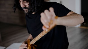 Idin Samimi Mofakham sitter på gulvet og stemmer et tradisjonelt strengeinstrument.