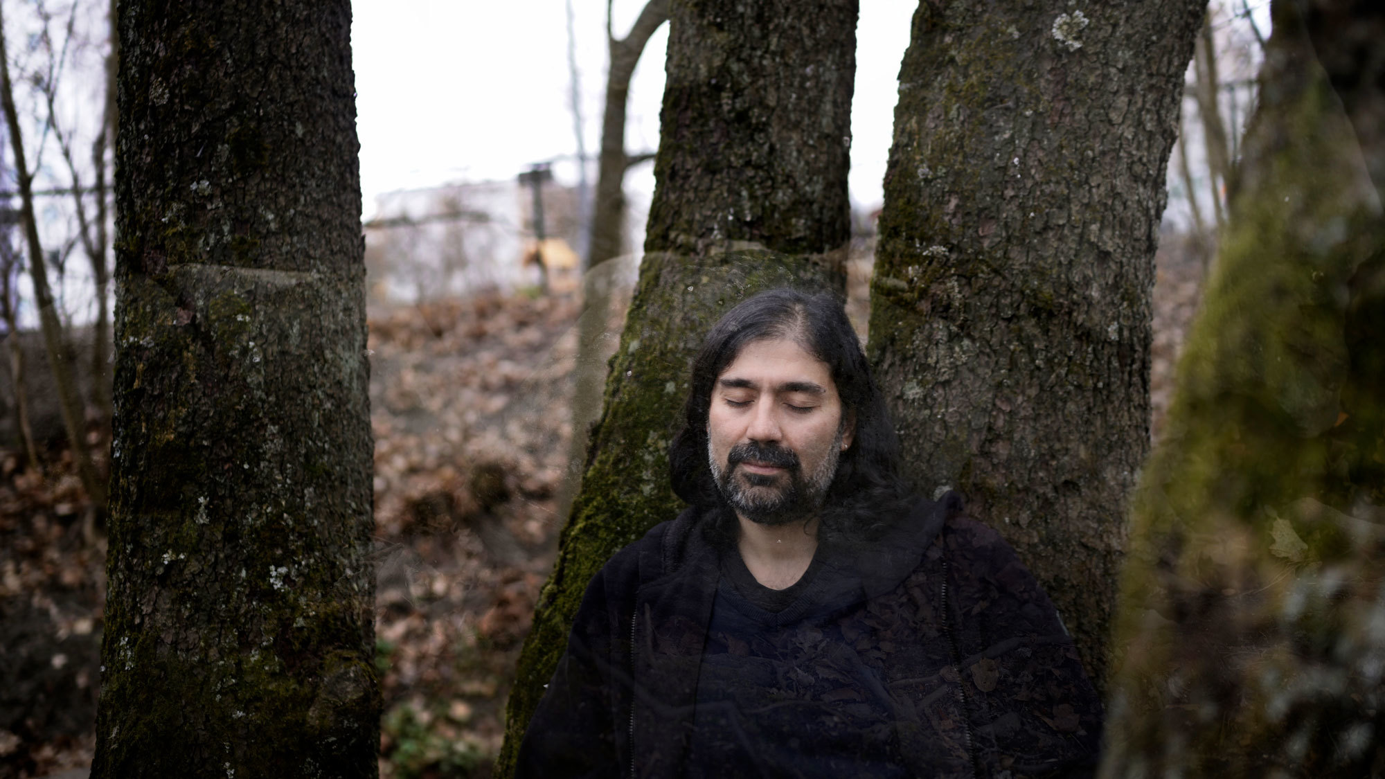 Idin Samimi Mofakham står mellom trær og lukker øynene.