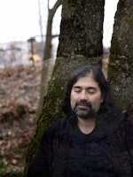 Idin Samimi Mofakham står mellom trær og lukker øynene.
