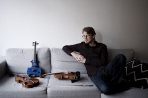 Jørgen Mathisen i grå sofa med tre fioliner ved siden av seg
