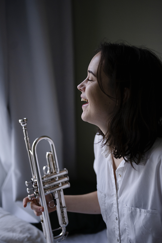 Kristna Fransson med trompet i hånda, ser mot vindu og ler