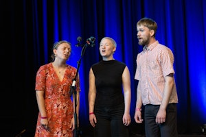 Tre sangere star rundt en mikrofon og synger