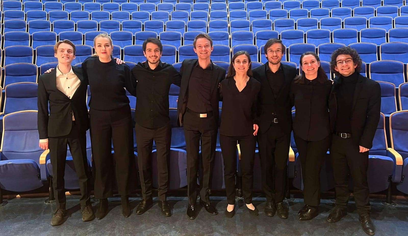 Alle dirigentene på NMH i 2023, står i svarte klær foran de blå stolene i Lindemansalen.