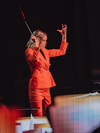 Hannah Howard i røde klær på dirigentpodiet med armene opp.