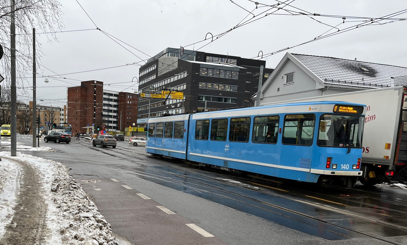 Blå trikk kjører ned Grefsenveien mot Storo-krysset. Vinter og våt asfalt.