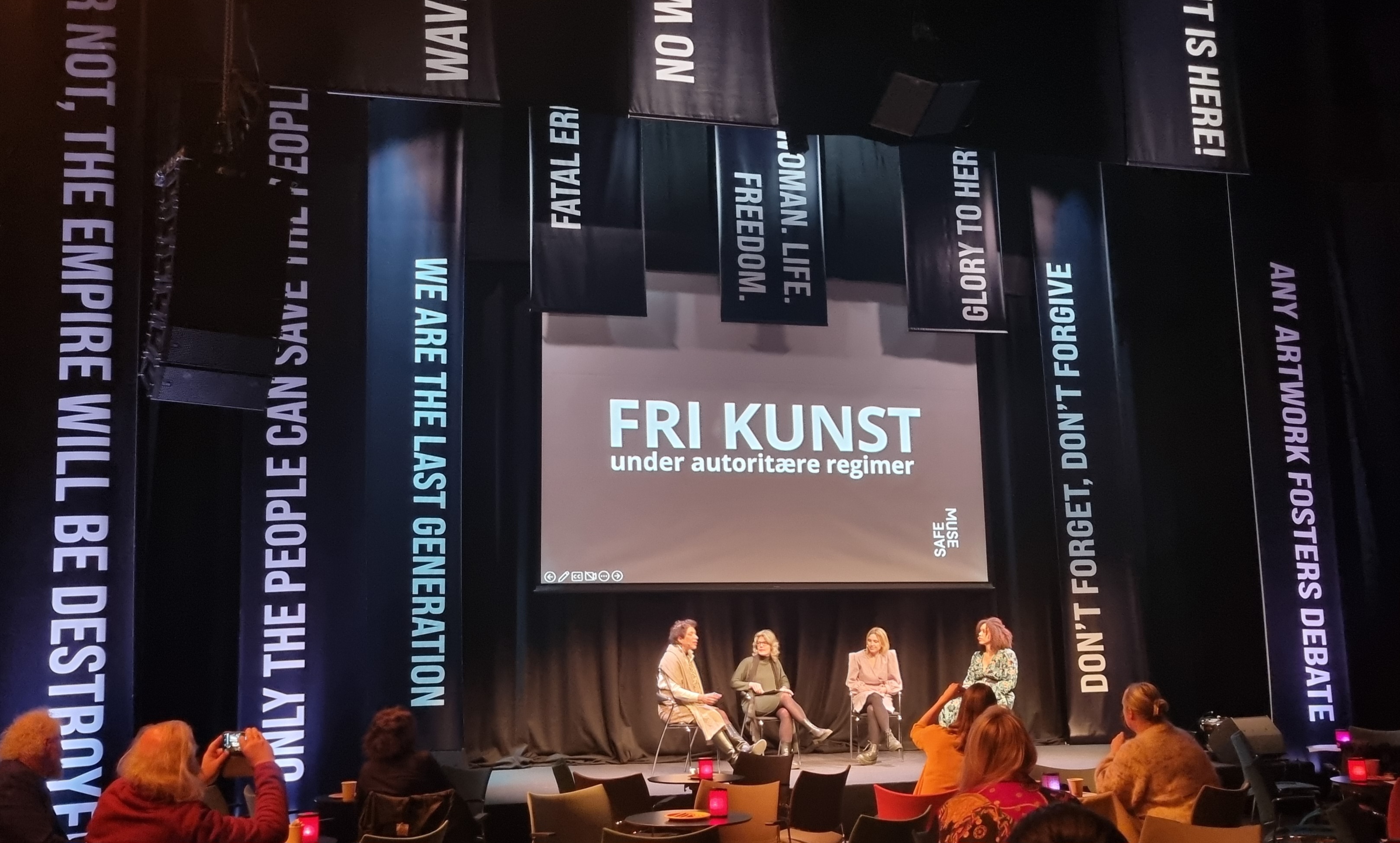 Astrid Kvalbein på scenen sammen med tre andre paneldeltakere. På veggen bak står det "Fri kunst under autoritære regimer"
