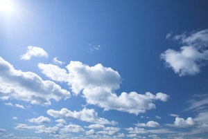Blå himmel med hvite skyer. Sola skinner inn i bildet fra øvre venstre hjørne.