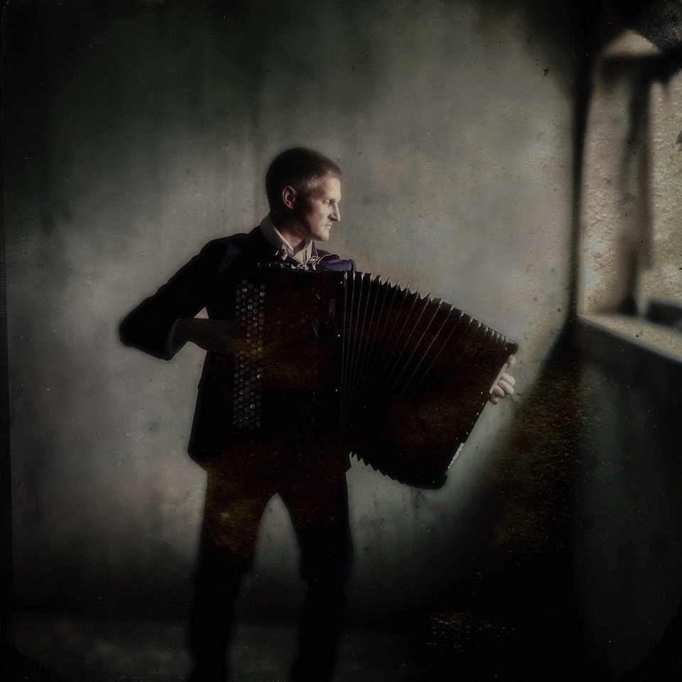 Silhuettbilde av Jo Asgeir Lie med trekkspill i et goldt rom.