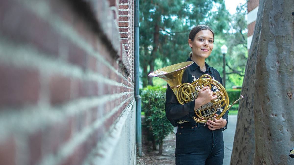 Siri Storheim står ved murvegg med hornet i hendene.
