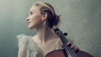 Portrett av Sophie Kauer i duse farger, der hun sitter med celloen og ser over sin høyre skulder.