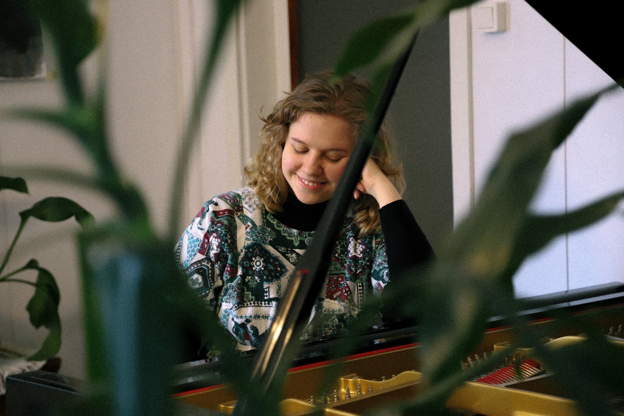 Siiri Ylijoki sitter ved flygelet og smiler, med en grønn plante foran seg.