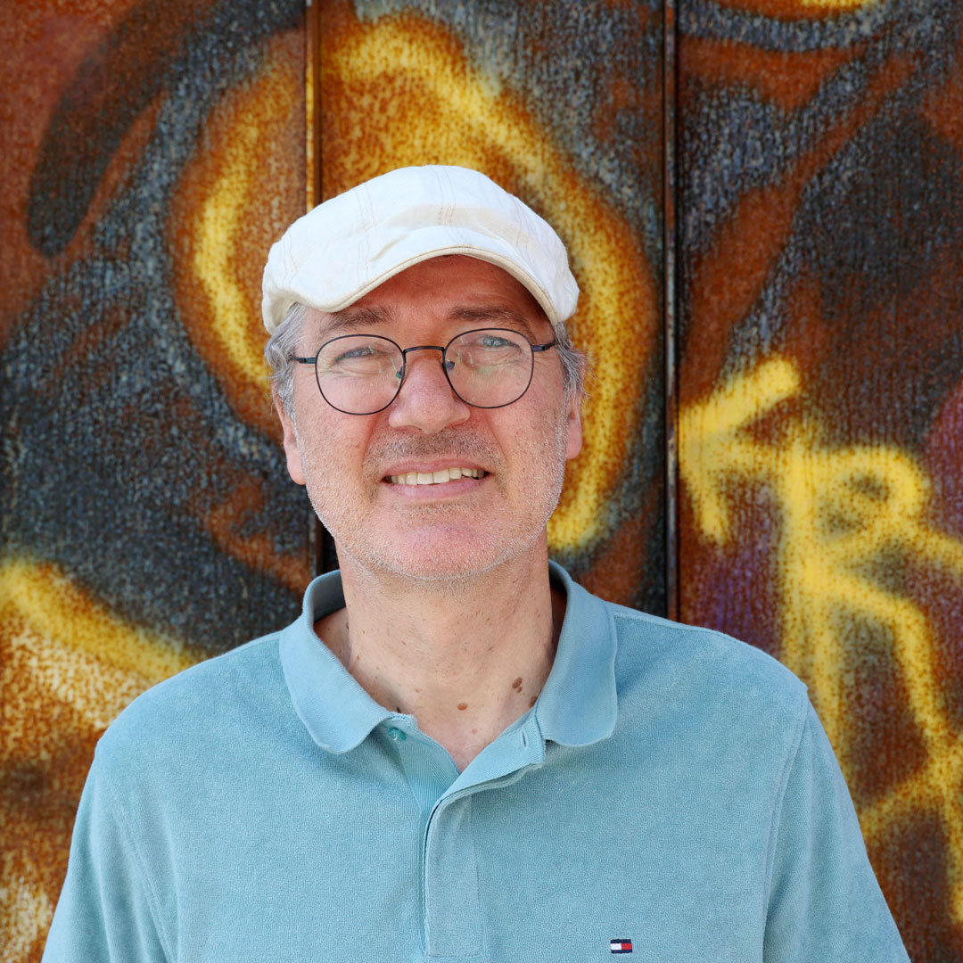 Knut Vaage står foran vegg med gul grafiti og smiler.