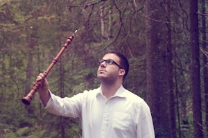 Lluis Calm Vidal står med en brun tre-obo mellom trærne i en skog og ser opp.