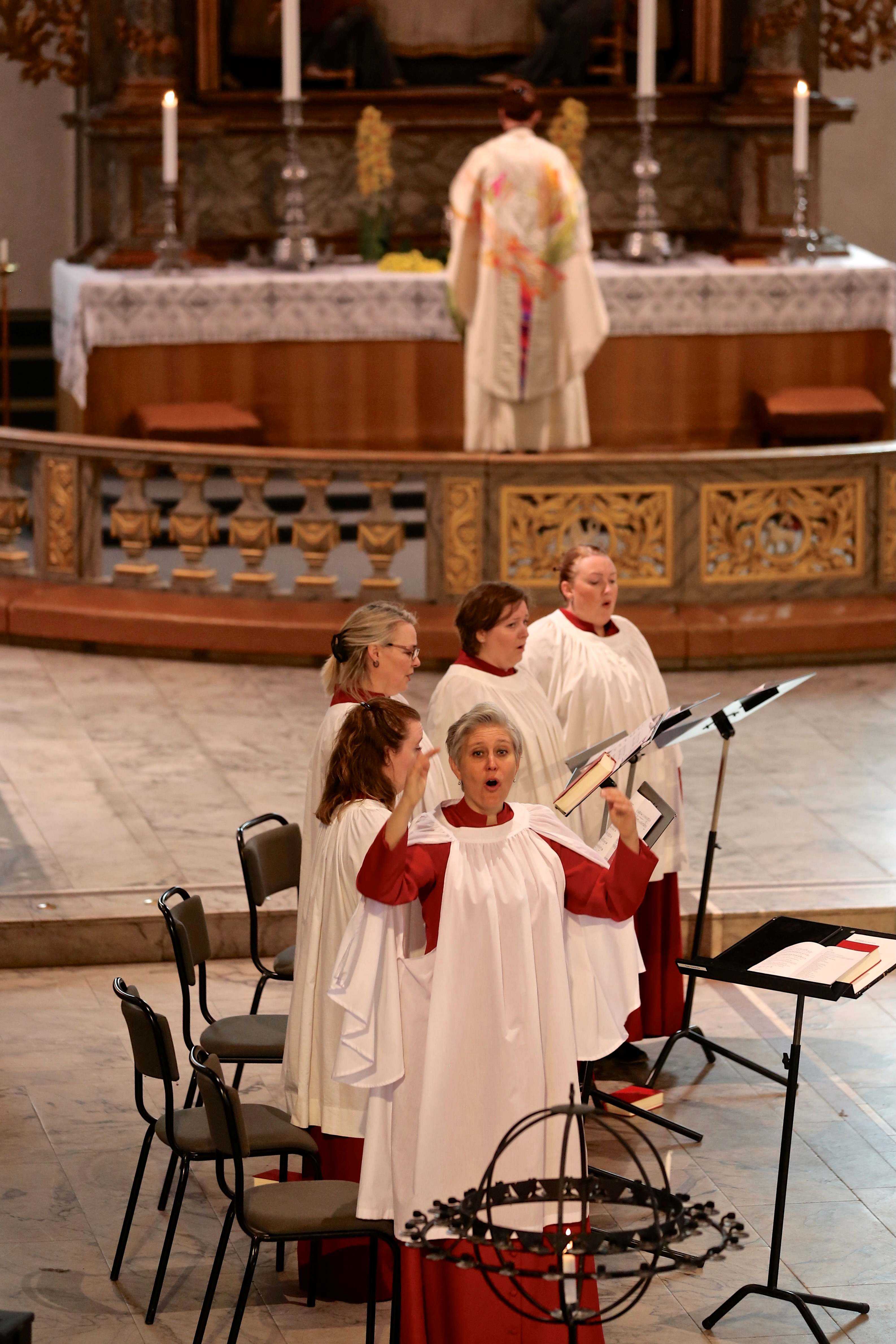 Dirigent og kirkesangere foran alteret i Oslo domkirke, med en prest i bakgrunnen.