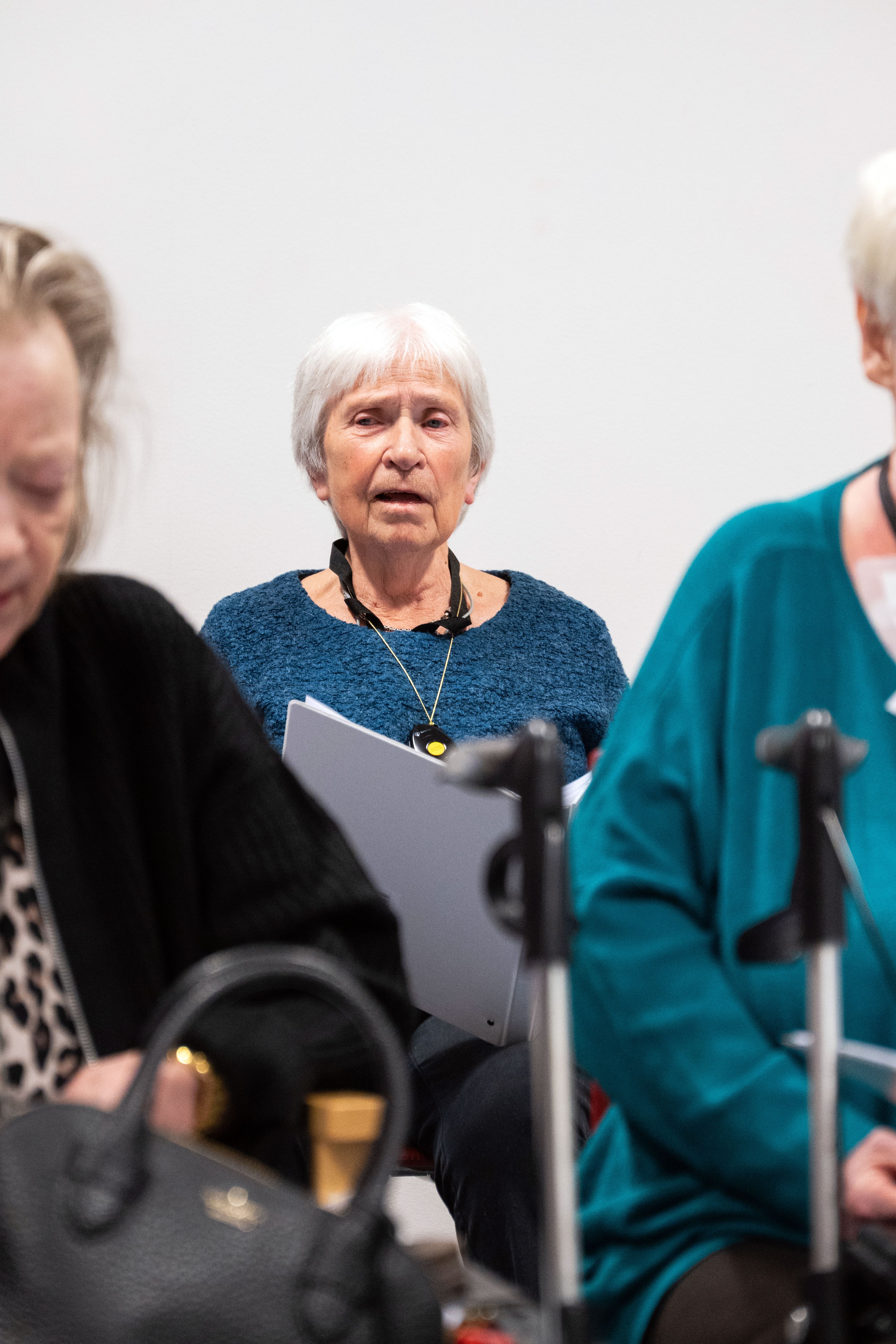 Eldre kvinne som synger i kor. Forgrunnen er uskarp med to korister og rullatorer.