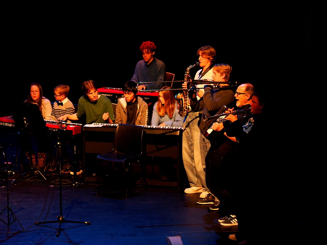 Unge og voksne musikere spiller forskjellige instrumenter sammen på en scene.