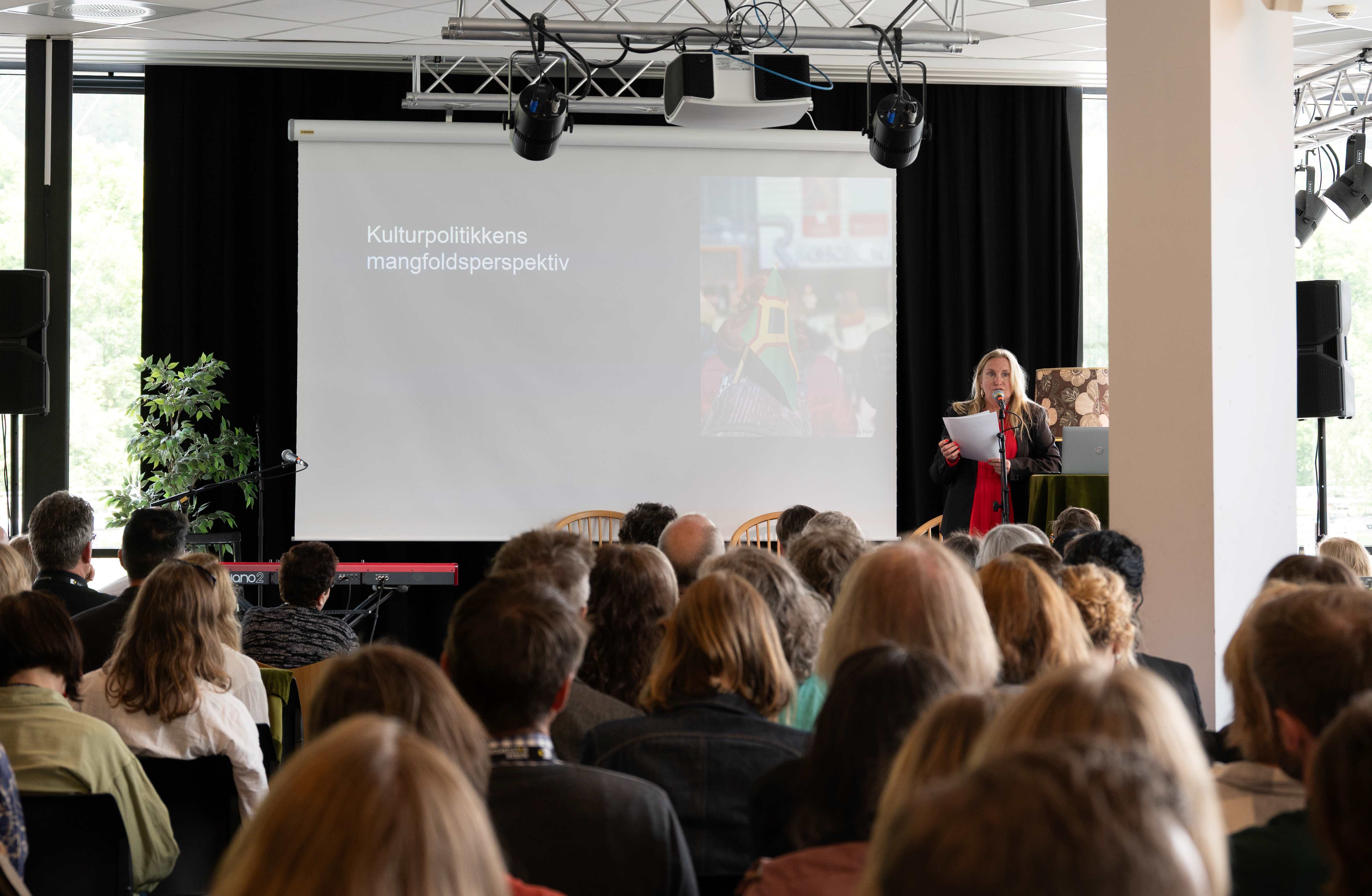 Sigrid Royseng står på en scene og snakker til en sal full av mennesker.