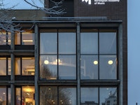 Den høyeste delen av NMHs fasade i mørket. Rett under taket står lyser logoen opp.