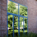 En av glassdørene ute på NMHs fasade. Det vårlige gresset speiler seg i døren.